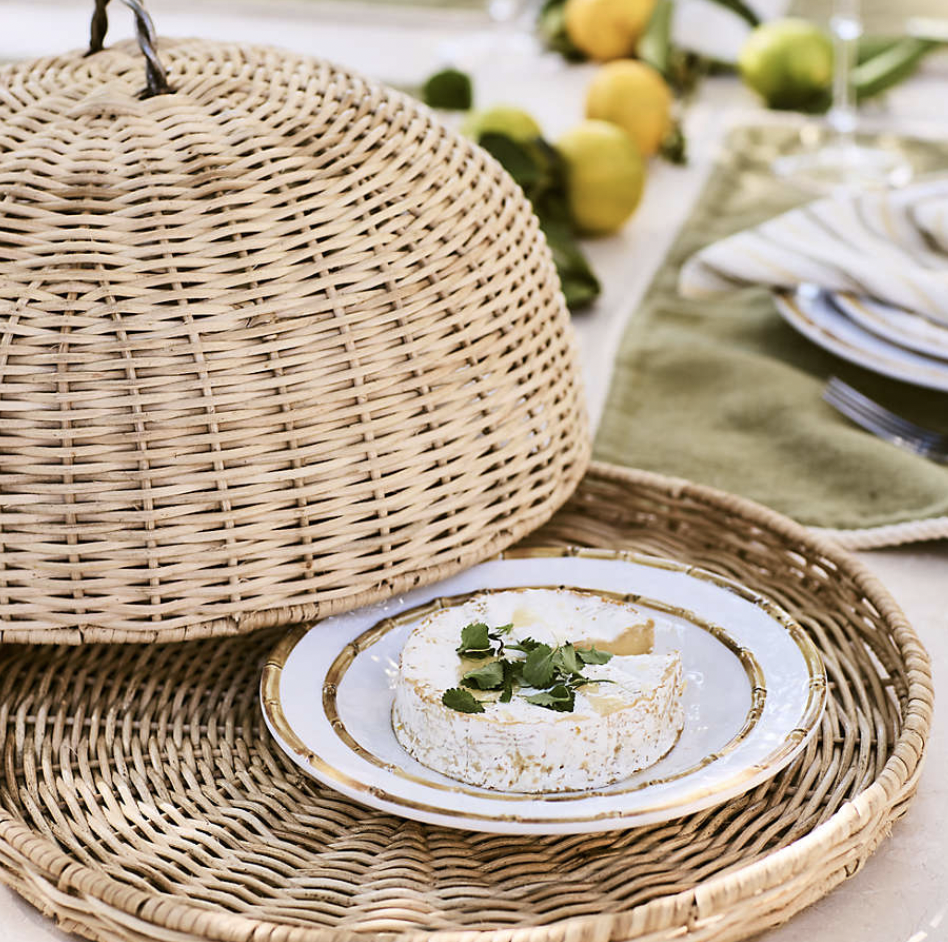 A natural rattan dome food cover with tray, used to keep dishes protected during outdoor dining.